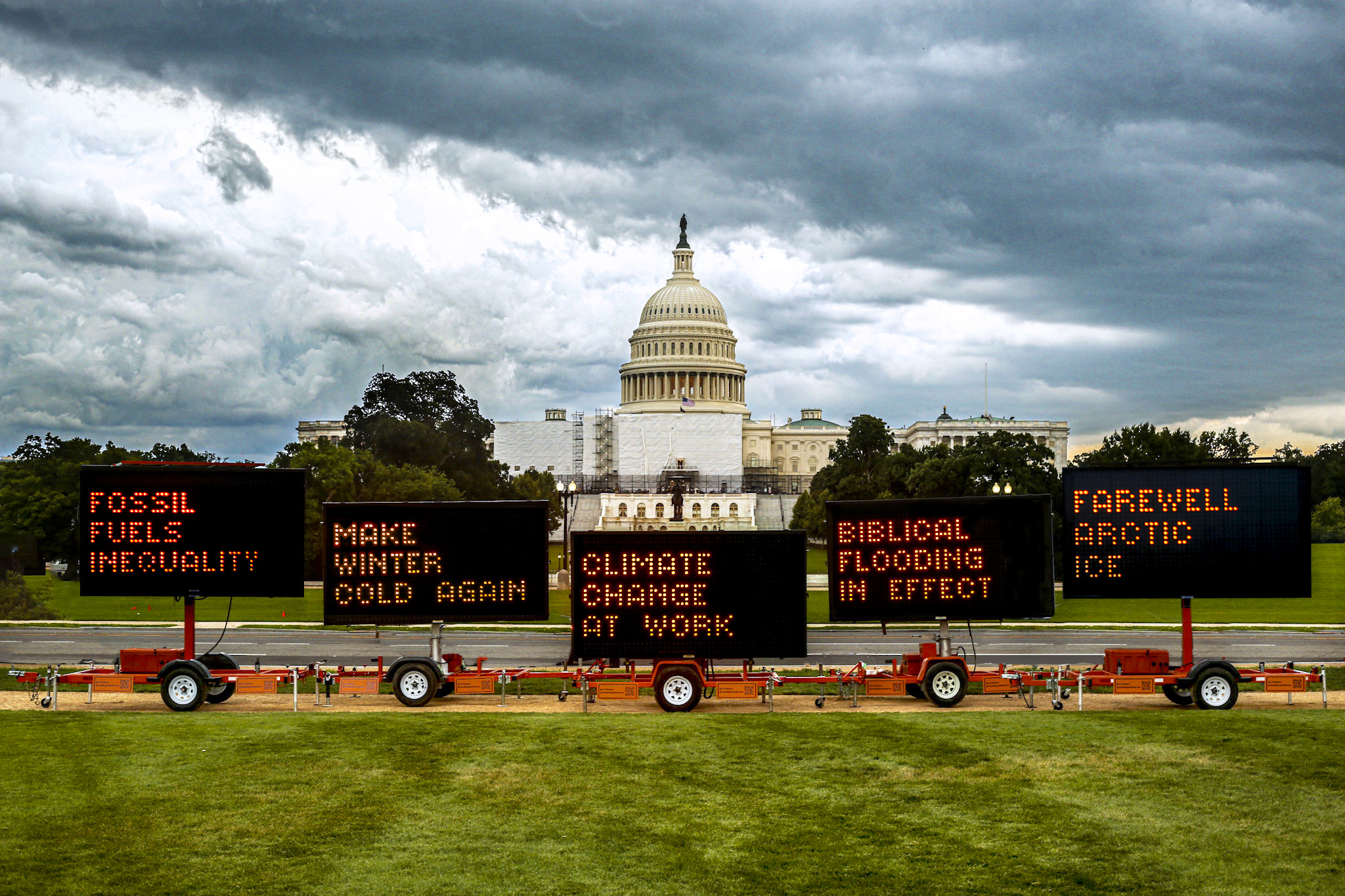 Washington DC Capital building with Justin Brice's public art exhibit of five solar-powered highway signs flashing texts calling attention to communities  impacted by extreme weather, environmental injustice, species extinction, and cautionary aphorisms about the devastating impacts of the climate crisis. 