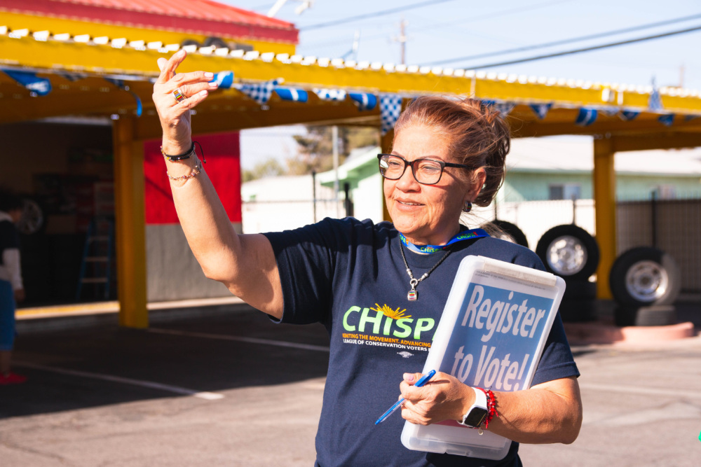 Chispa employee holding a sign that says "Register To Vote" and waving someone to them.