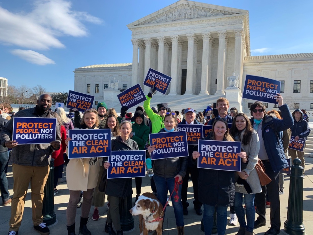 Staff holding signs that read "Protect People Not Polluters" and "Protect The Clean Air Act" while standing outside the Supreme Court building