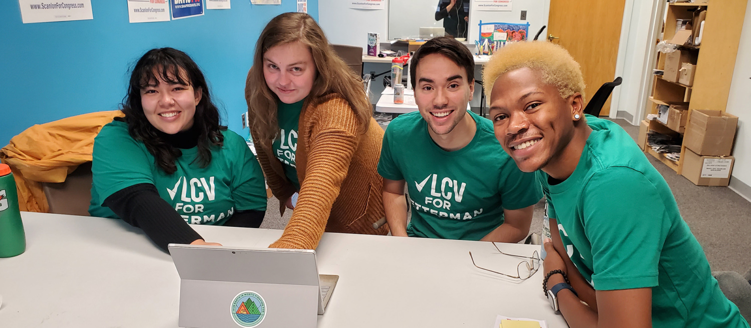 A group of campaign staff huddled around a table wearing LCV for Fetterman shirts.