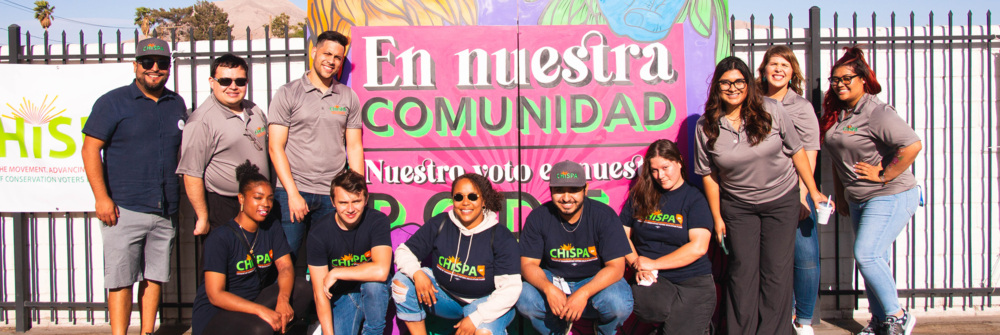 Chispa staff pose in front of sign about voting.