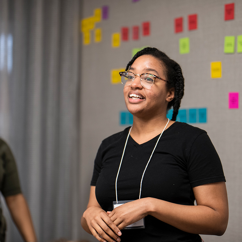 Young person standing in front of a wall of sticky notes at a leadership training.