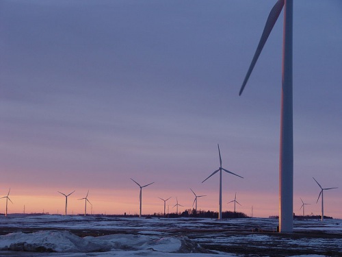 Wind turbines are shown against a sunset.