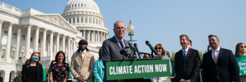 Senate Majority Leader Chuck Schumer speaks at a podium during a Climate Action Now press event in front of fellow lawmakers and the Capitol building in DC