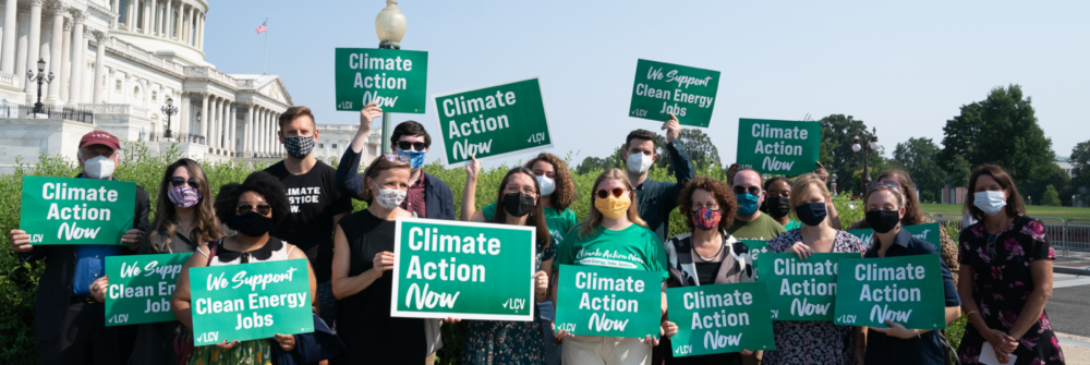 LCV staff hold signs that read "Climate Action Now" and "We Support Clean Energy Jobs" in front of the Capitol building in D.C.