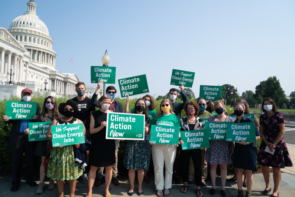 LCV staff hold signs that read "Climate Action Now" and "We Support Clean Energy Jobs" in front of the Capitol building in D.C.