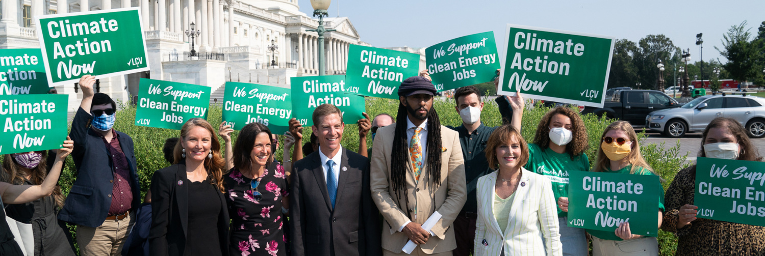 A group of people and representatives holding signs reading "Climate Action Now" in front of the U.S. Capitol.