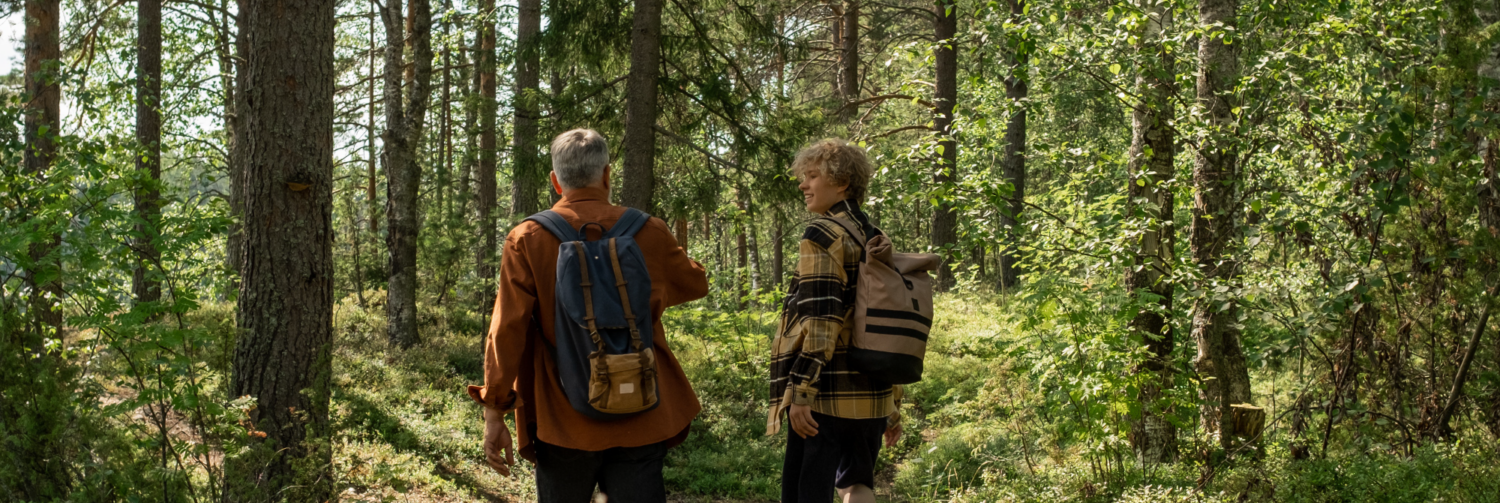 A father and his teenage son hike on a trail through a forest