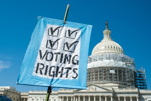 Foreground; A sign with four checkmarks that reads "Voting Rights" Background: The Capitol building under construction