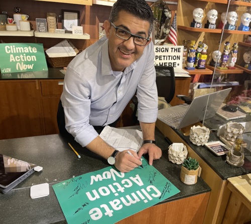 A community member and store owner signs a Climate Action Now sign in his store