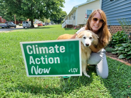 An LCV supporter poses with her "Climate Action Now" yard sign and dog in her front yard