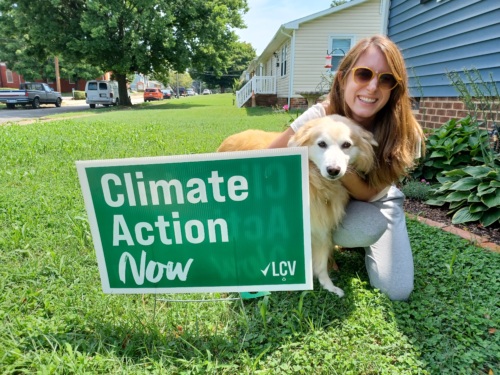 An LCV supporter poses with her "Climate Action Now" yard sign and dog in her front yard