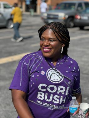Representative Cori Bush smiles in a parking lot while wearing her campaign T-shirt.