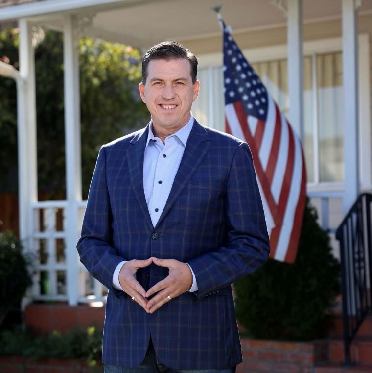 Representative Kevin Mullin stands outside a house with an American flag.