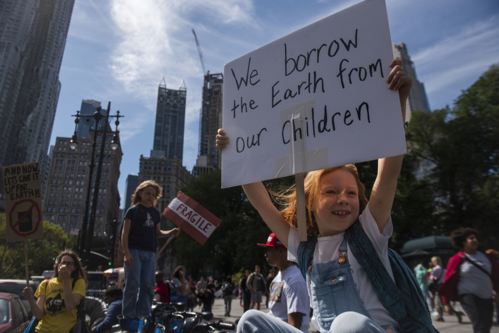 A young girl holds a sign that reads, "We borrow the Earth from our children" at a rally.