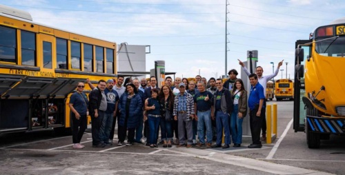 A large group of Chispa activists poses with two electric school buses.