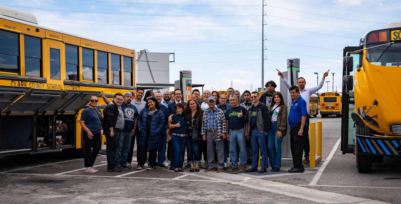 A large group of Chispa activists poses with two electric school buses.