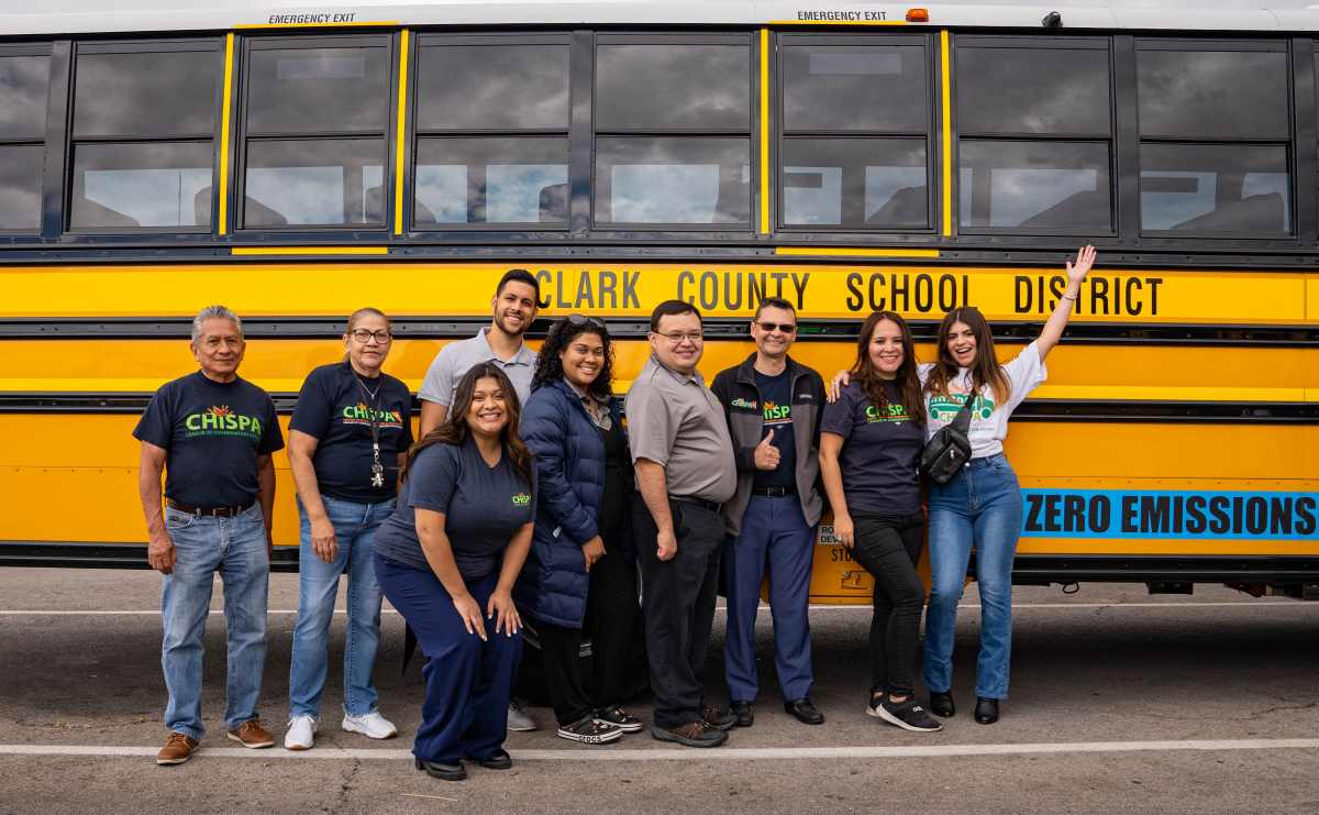 A group of Chispa activists pose in front of a Clark County electric school bus.