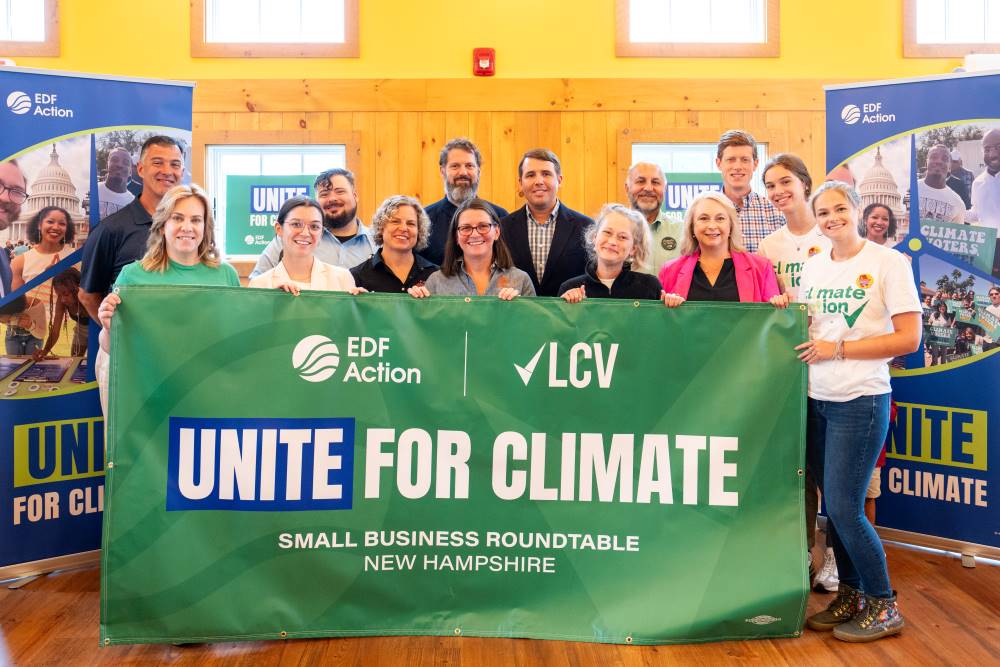 Smiling faces hold up sign that has the EDF Action and LCV logos on them and reads: "Unite for Climate" and "Small Business Roundtable, New Hampshire"