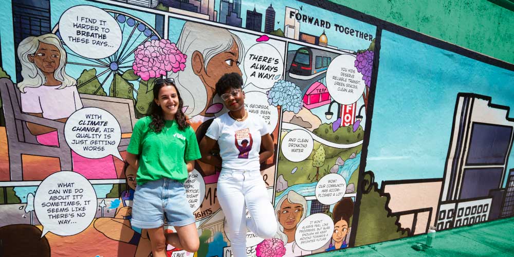 Two people pose in front of the new mural, which depicts a comic-book style history of activism in Georgia.