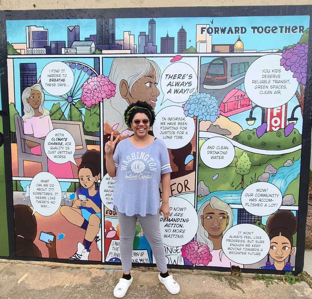 Artist Caitlin Rogers stands in front of their mural. 