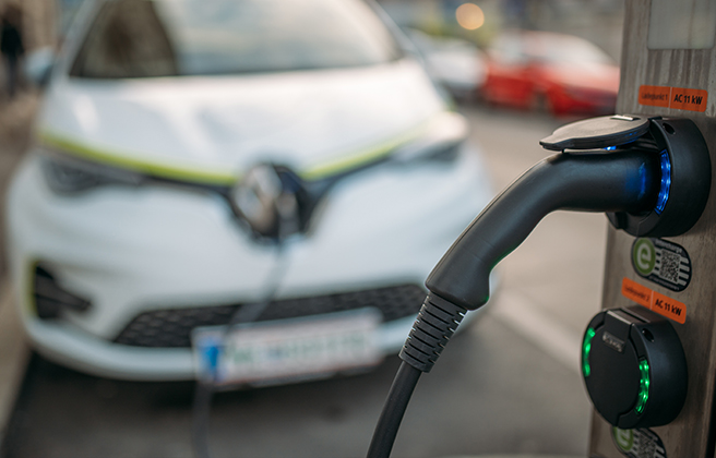 Electric vehicle charging port close up with vehicle in background.