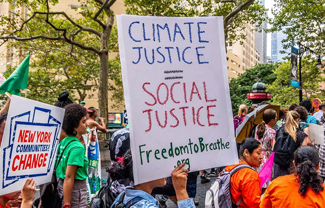 Activist marching in climate protest holding sign that reads “Climate Justice = Social Justice”.