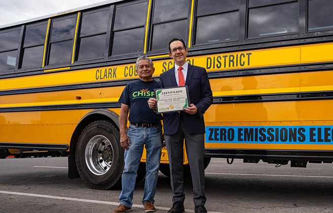 Two people standing in front of newly commissioned electric school bus.