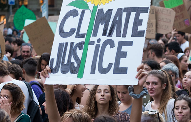 A young person holding a sign at a march that reads “Climate Justice”.