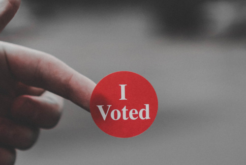 Closeup of a person holding an “I Voted” sticker on their finger.