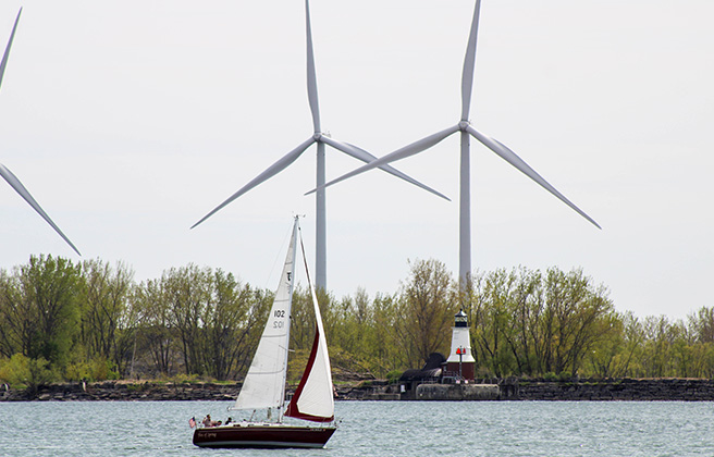 A sailboat passes a lighthouse and wind turbines as it enters Lake Erie at Buffalo, New York.