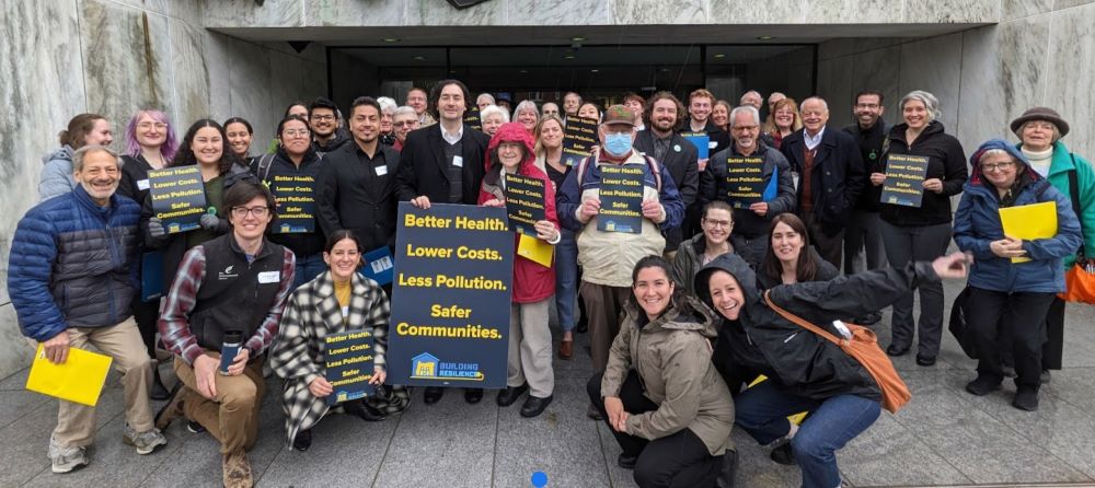 Group of activists posing with a sign reading "Better Health, Lower Costs, Less Pollution, Safer Communities"
