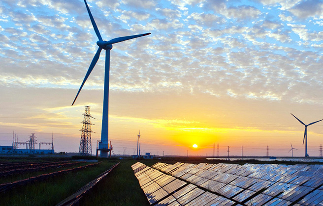 A wind turbine towering over rows of solar panels.