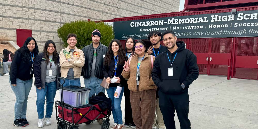 A group of people smiling at the camera stand in front of a sign that reads Cimarron-Memorial High School.