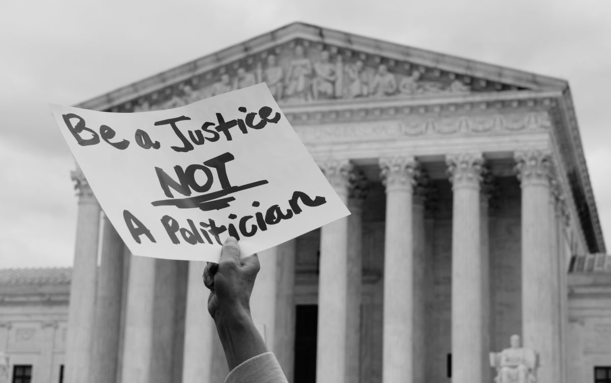 A sign reading "Be a Justice NOT A Politician" is held up in front of the Supreme Court building.