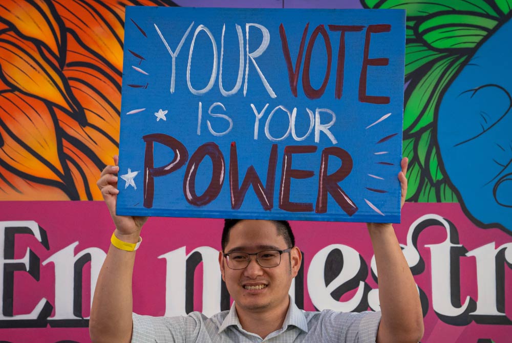 A man holding a sign up that reads “Your Vote Is Your Power”