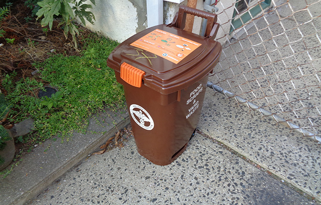 Closeup of a brown compost bin in someone’s driveway.