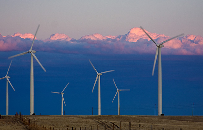 A wind farm with the sun setting on clouds behind.