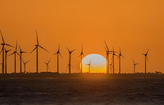 Orange sunset behind a row of wind turbines.