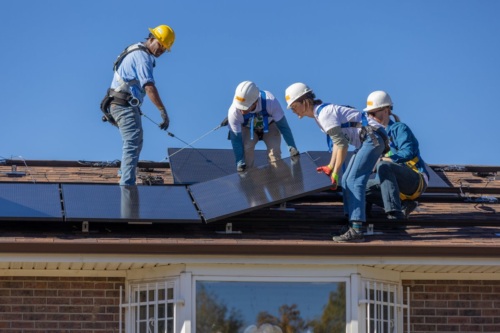Team of four men and women installing solar panels on the roof of a house.
