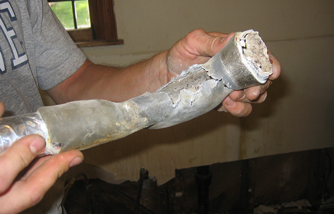 Person holding a section of a lead water pipe removed from their house.