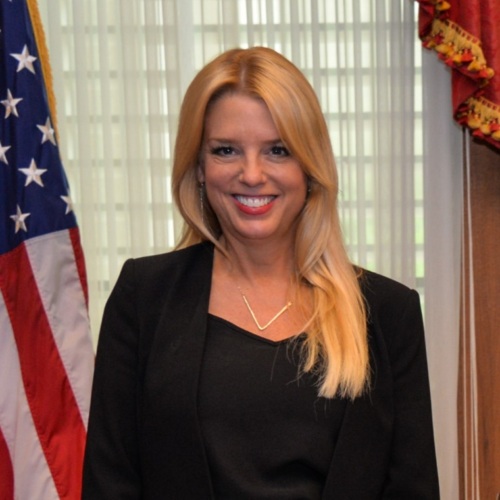 Pam Bondi poses in front of a window and an American flag