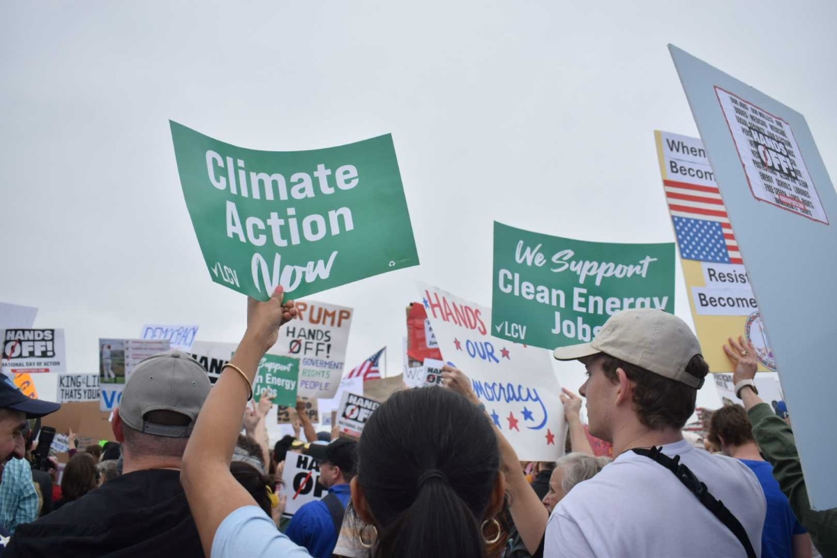 Protesters hold up green LCV-branded signs reading "Climate Action Now" and "We Support Clean Energy Jobs."