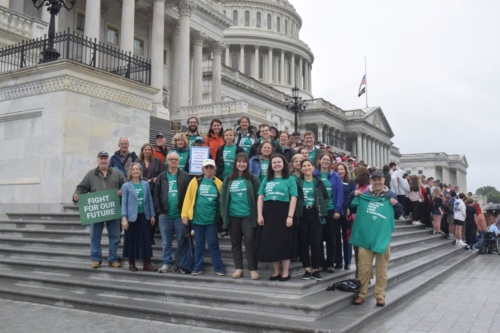 A group of over 20 people in green t-shirts pose on the Capitol steps, with a sign reading "Fight for Our Future."