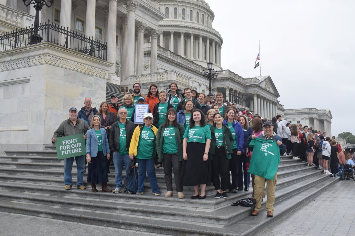 A group of over 20 people in green t-shirts pose on the Capitol steps, with a sign reading "Fight for Our Future."