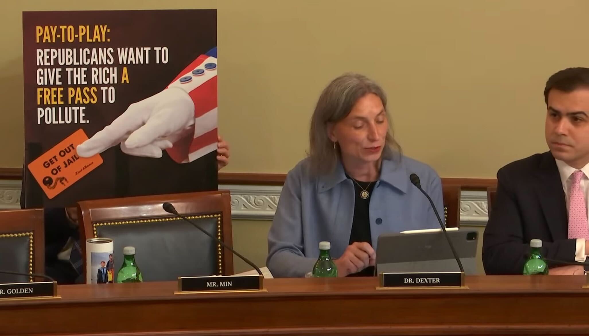 Rep. Maxine Dexter with a poster reading "Pay-to-Play: Republicans want to give the rich a free pass to pollute."