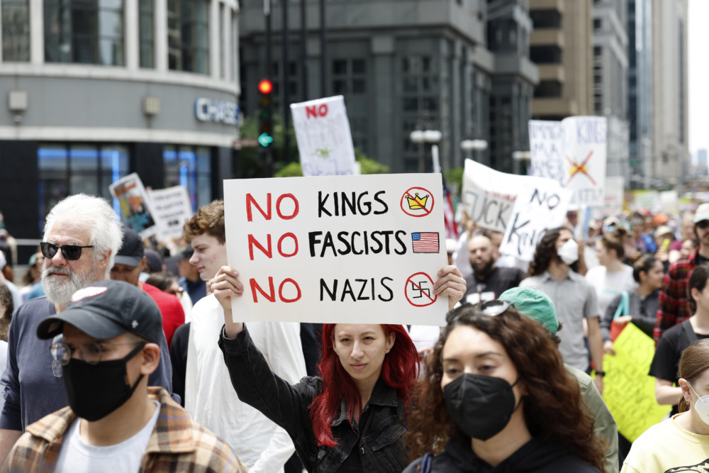 A protester carrying a sign that reads "No kings, no fascists, no Nazis" in a large crowd.