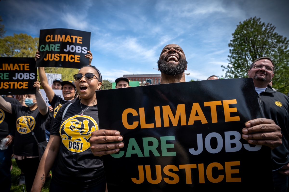 A group of protestors wearing black shirts and holding signs reading "Climate, Care, Jobs, Justice"