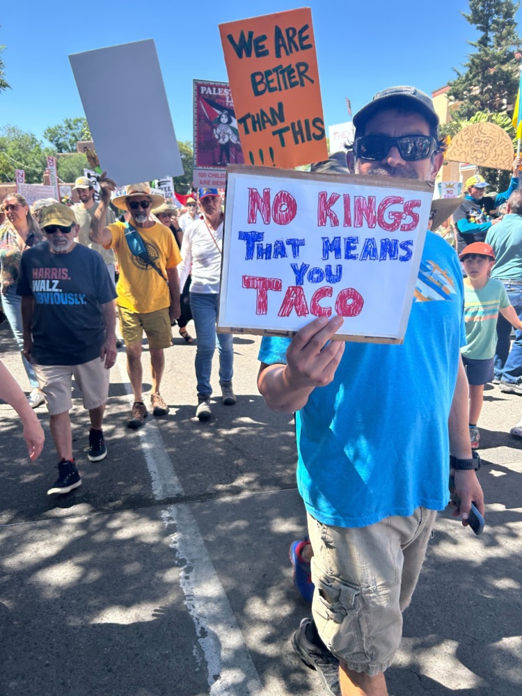 A protester in a crowd holds a sign that reads, "No Kings- that means you TACO."