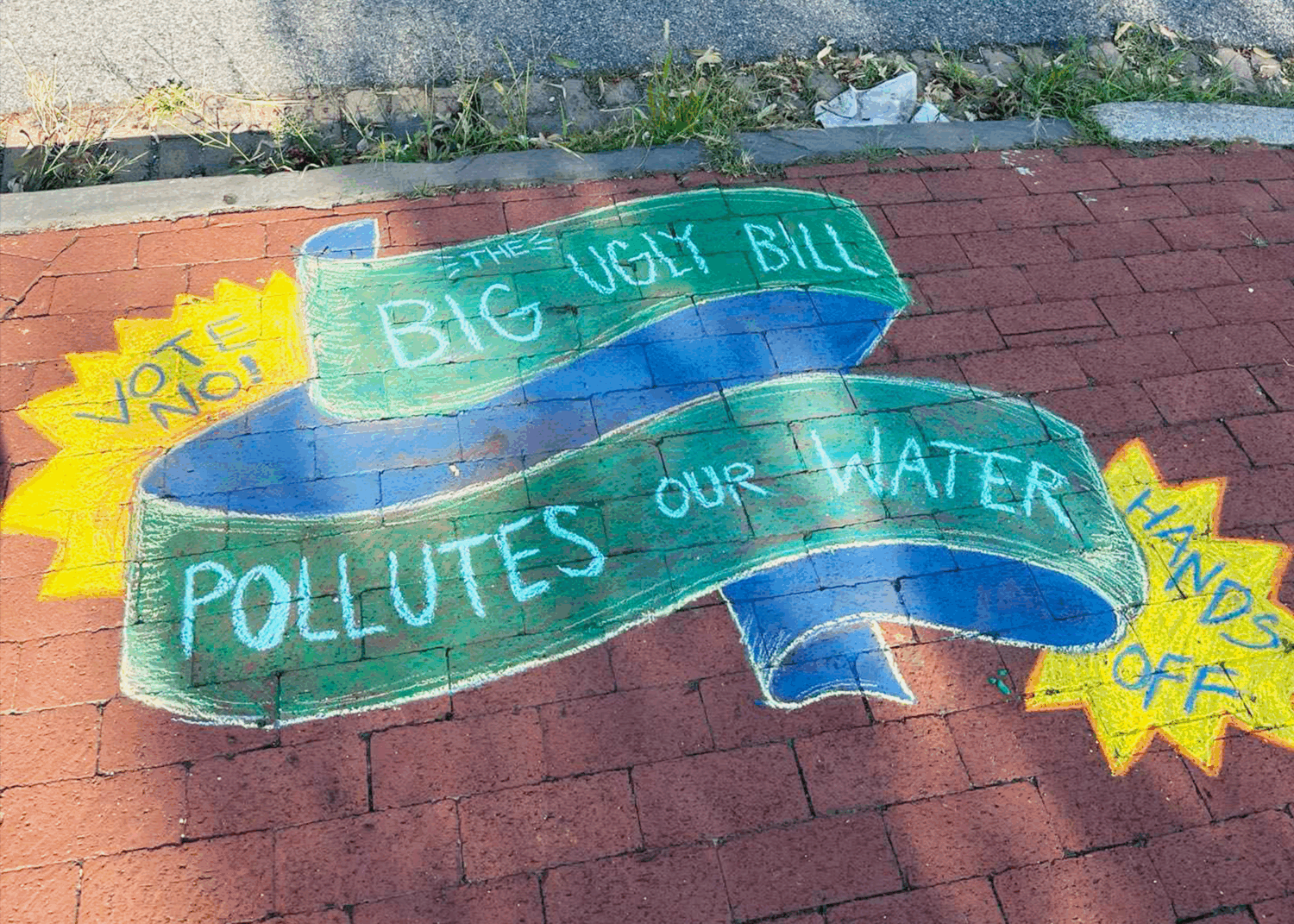A chalk mural that reads “The Big Ugly Bill polluters our water,” “Vote no!,” and “Hands off.”
